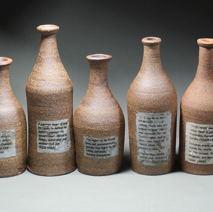 12 various sizes brown clay jugs and 2 chalices. The jugs have a piece of paper plastered on the front of them with a short blurb of text on it.