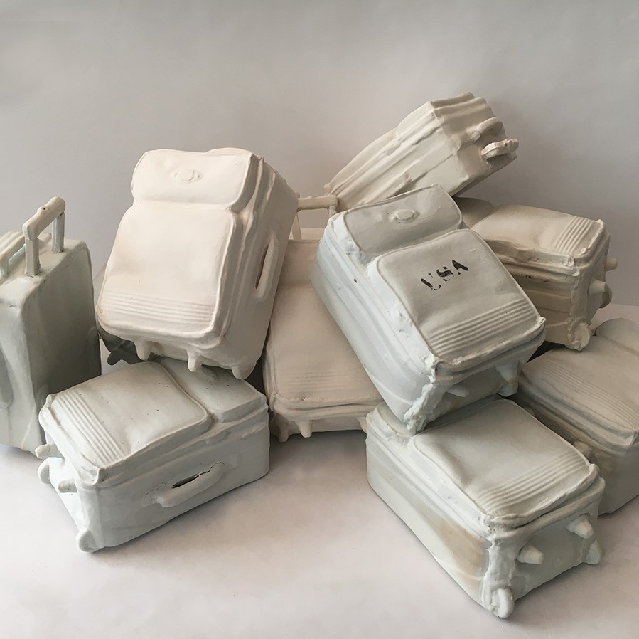  a sculpture of a pile up of suitcases. They are all white. One suitcase has 'USA' stamped on it in black.
