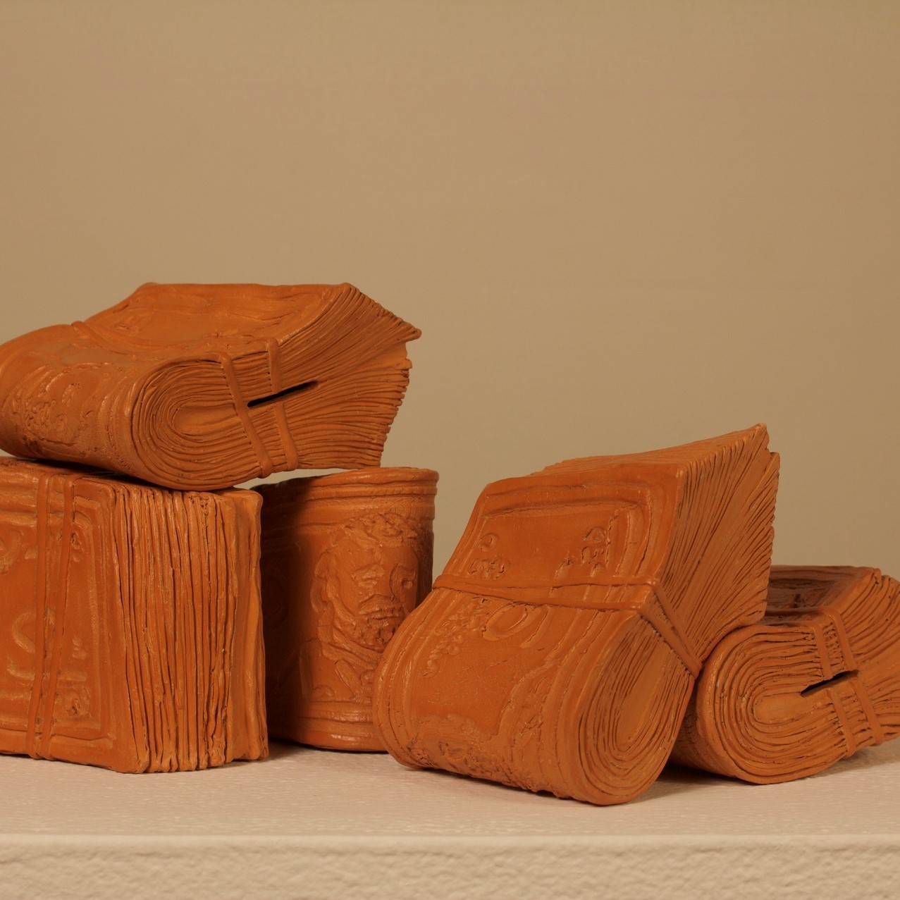 burnt orange colored clay sculptures that look like wads of cash rubber banded together. There are 5 different 'wads' of cash made of clay sitting around and resting on each other.