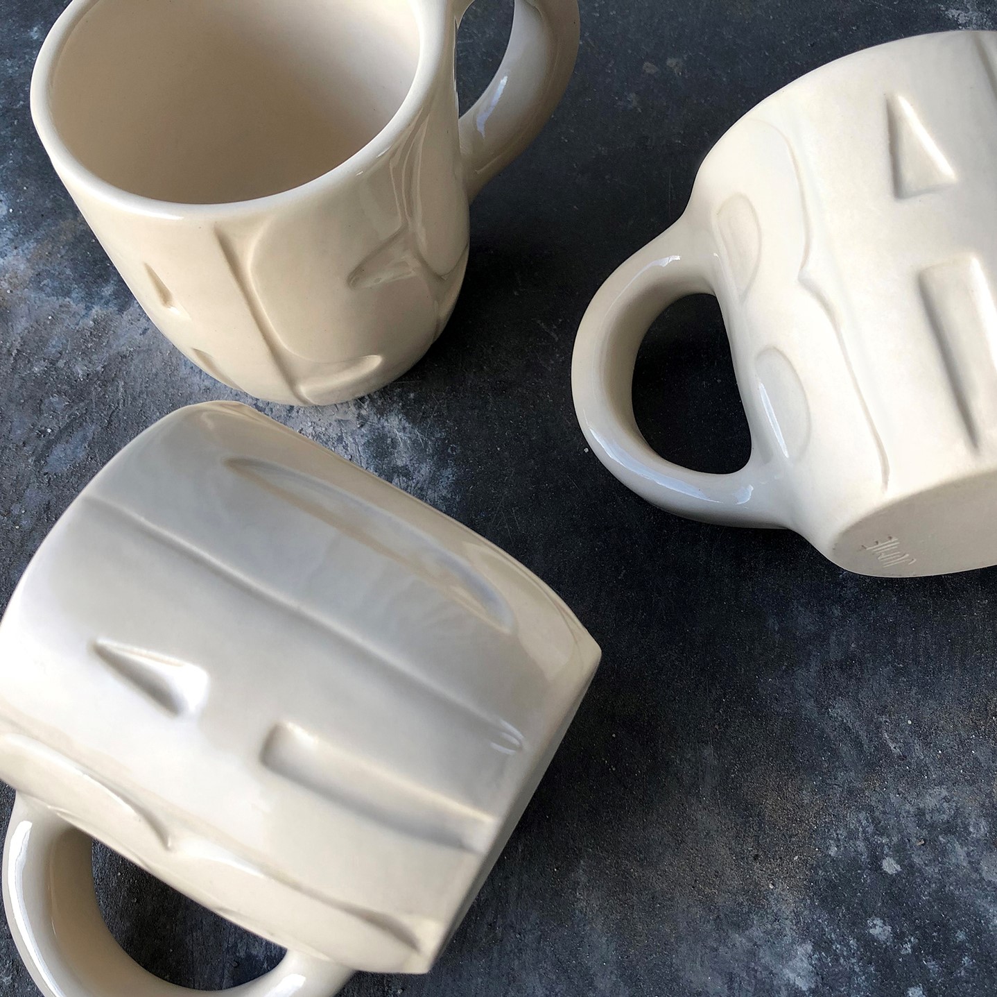 three cream colored coffee mugs with the word 'badass' carved into the outside of the mugs.