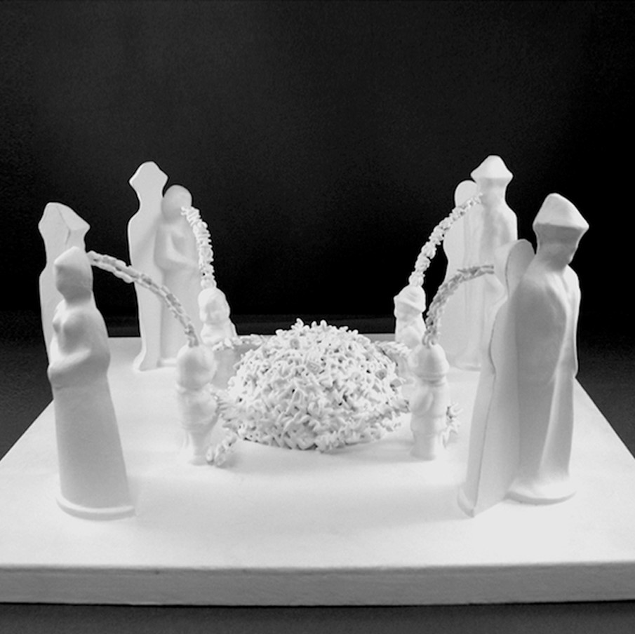 white sculpture of adult figures standing on a square base in the four corners. There are words coming out of their mouths in a stream. The streams each land on a childs head that stands in front of each of the edults. There is a pile of words and letters in the center.