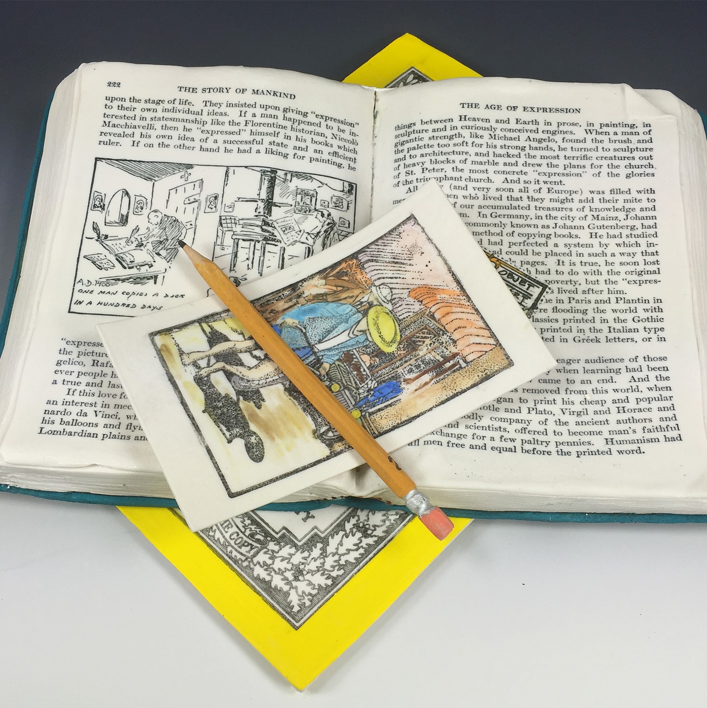 An open book sitting on a magazine or book with a bright yellow border. A postcard and pencil sit on top of the book. This is all made of clay.