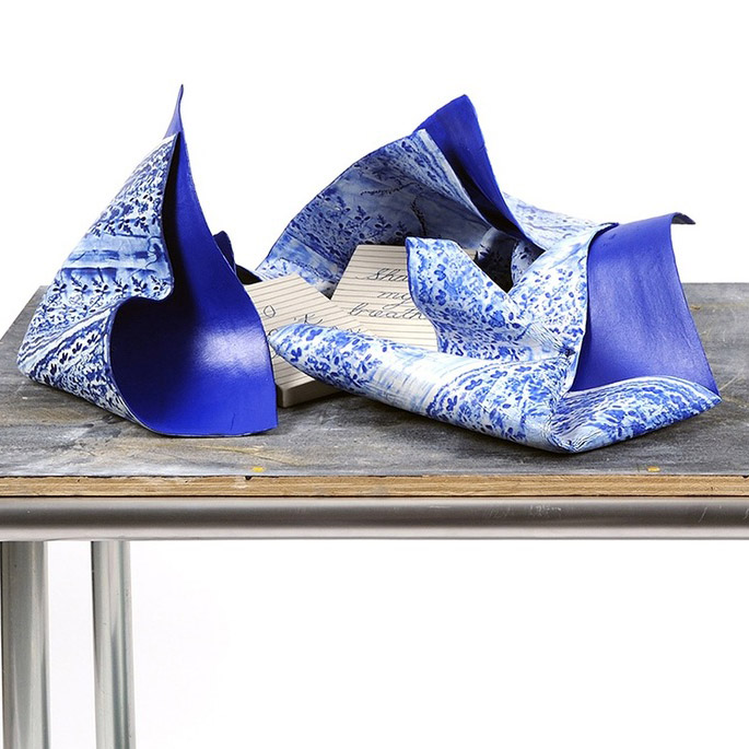 table that looks like it would be in a professional kitchen. On the table rests three pieces of blue cray that are shaped and painted to resemble bandanas. There are two note cards with cursive writing on them in the bandanas. One reads 'I can't breate' and the other says 'Share my breath'