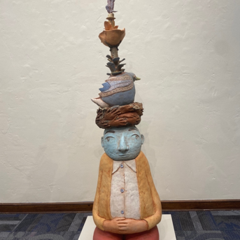 Benevolent Spirit: Image Description: Statue of man sitting with objects stacked on head.
