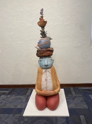 Benevolent Spirit: Image Description: Statue of man sitting with objects stacked on head.