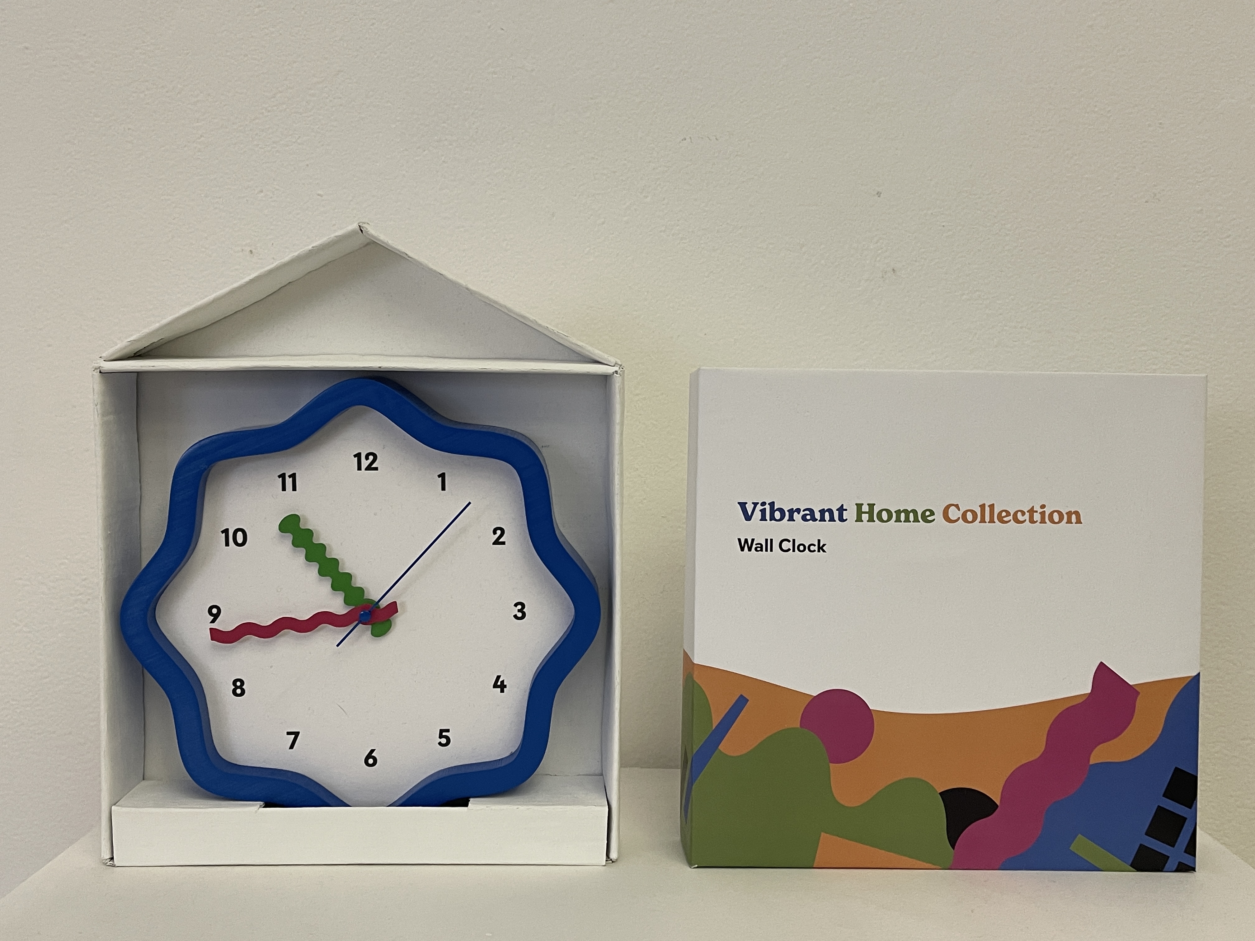 A photograph of a blue wall clock next to its packaging