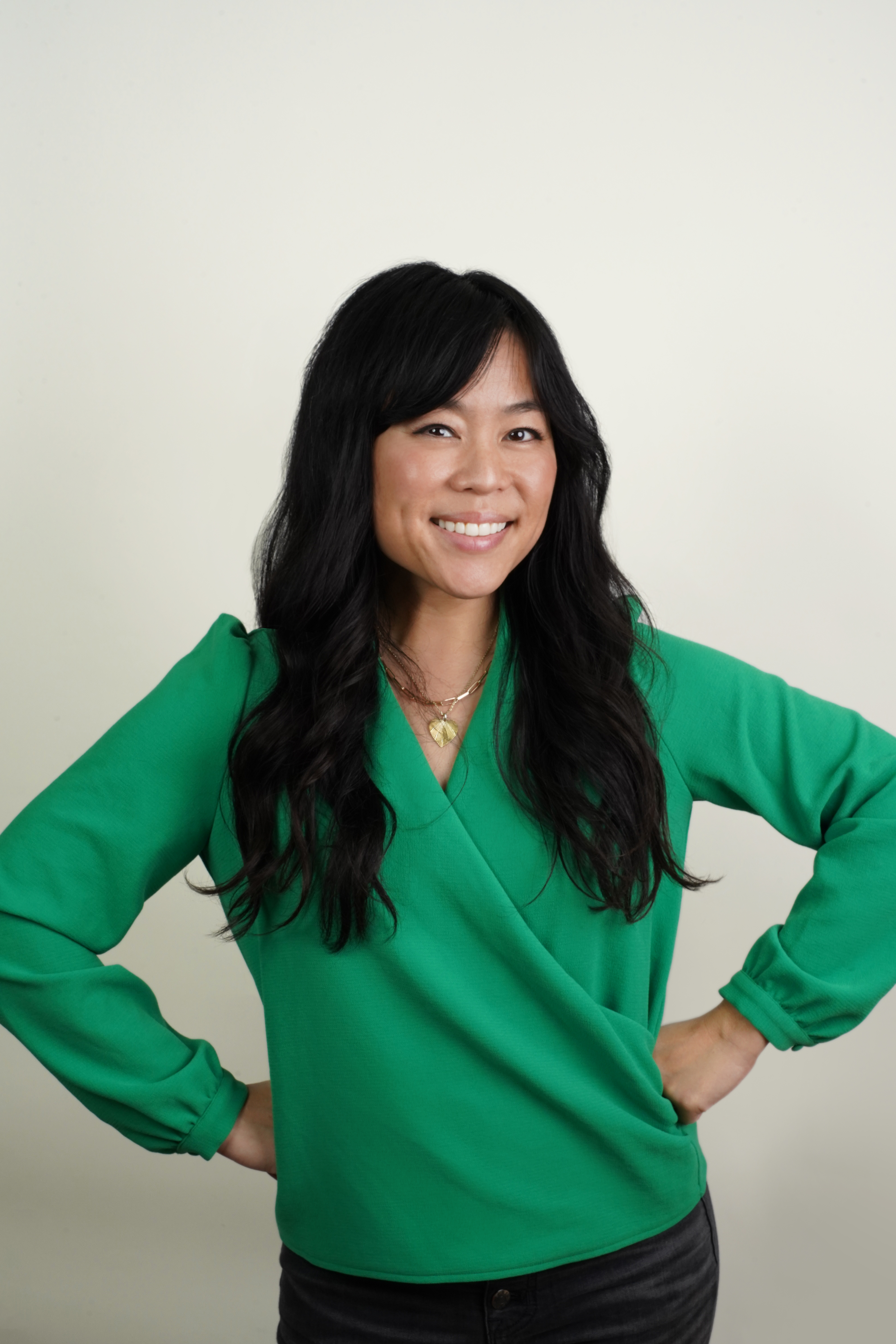A picture of Danielle Takata in a green long sleeve shirt with her arms at her waist in front of a white background.