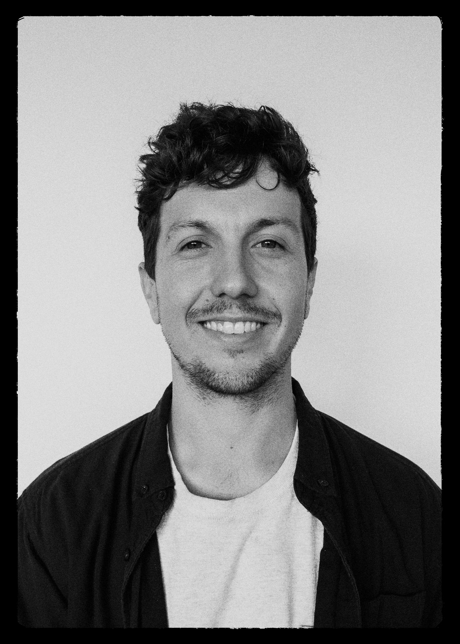 A black and white photograph of Jared Boyle. He is smiling, and looking straight at the camera.