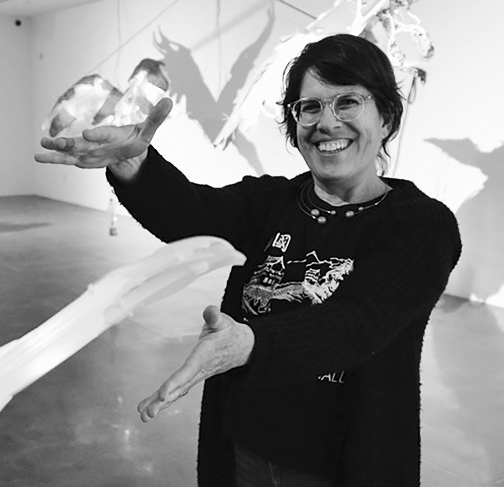 black and white photo of cynthia smiling at the camea next to her art work