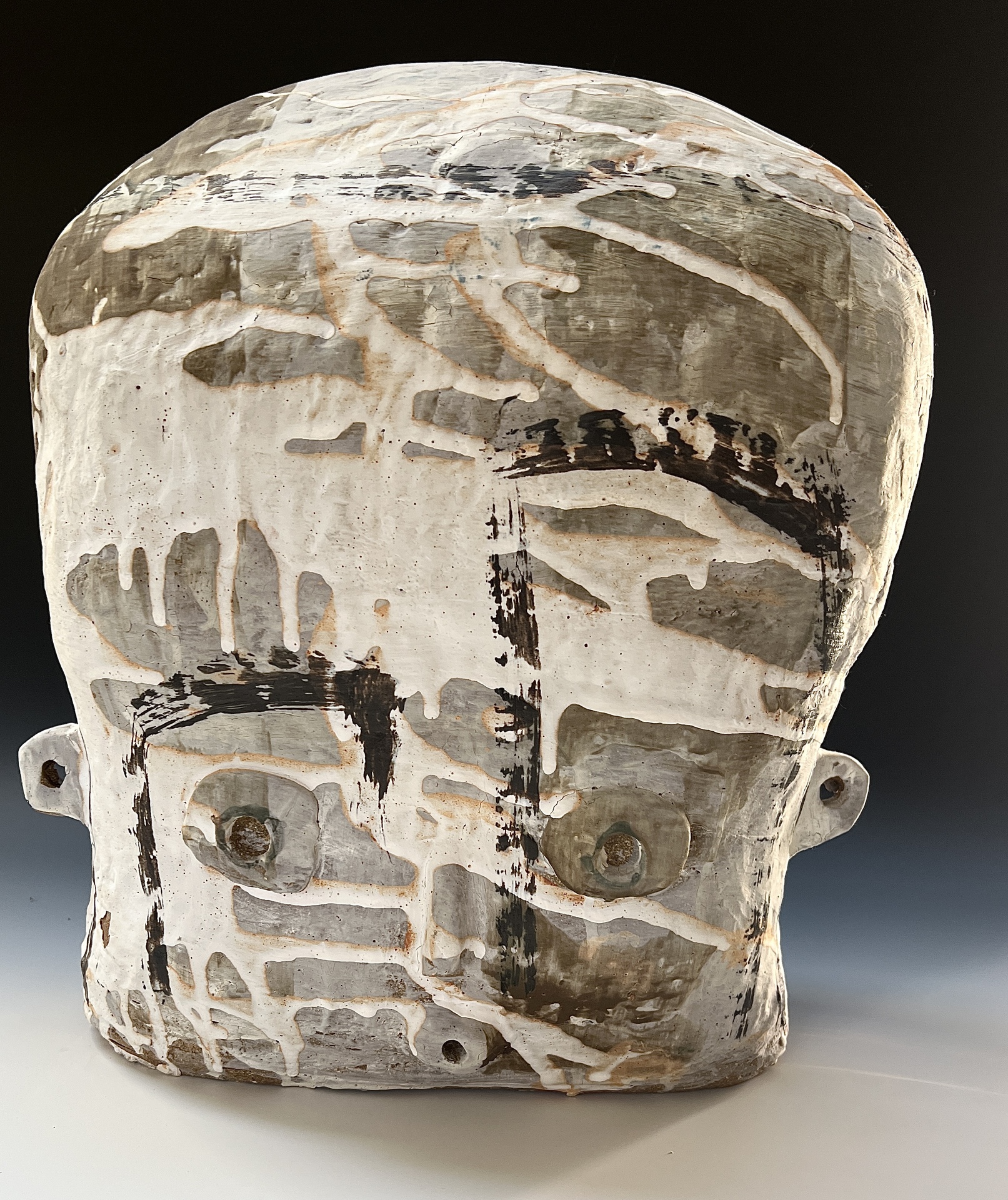A large, abstract ceramic sculpture resembling a human face, with rough, layered textures and muted earth tones, featuring expressive brushstrokes and incised lines that highlight facial features in a stylized manner.