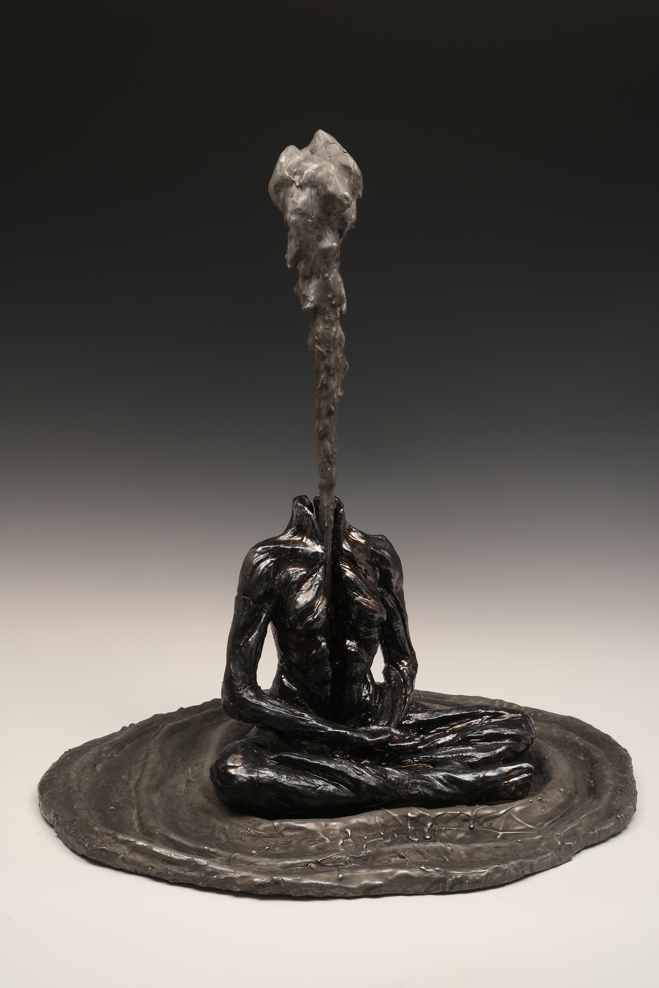 A dark, contemplative sculpture of a seated, headless figure with water rising from its neck, creating an ethereal effect.