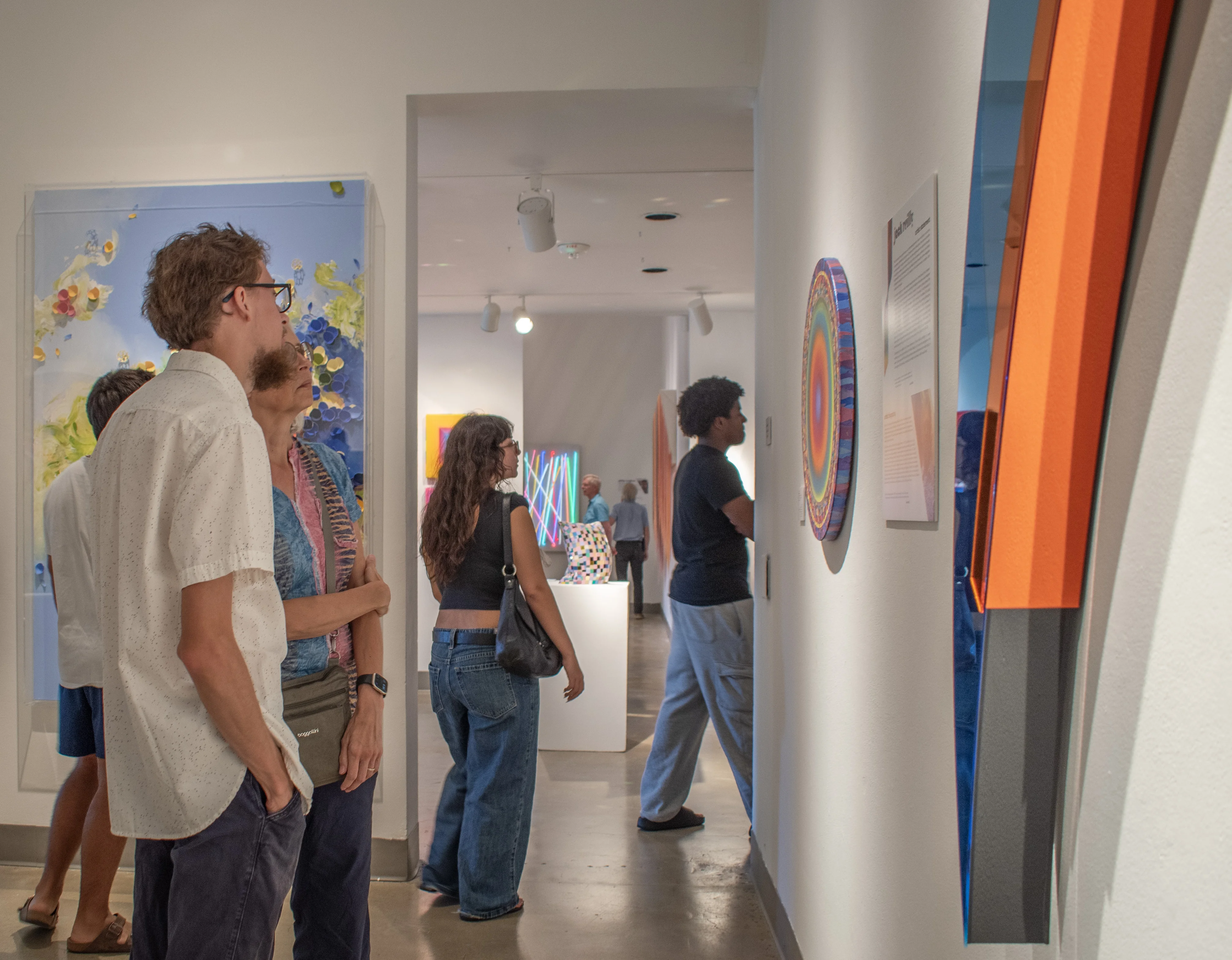 A group of visitors stand before the artwork of Seda Saar, Jack Reilly and Larisa Safaryan.
