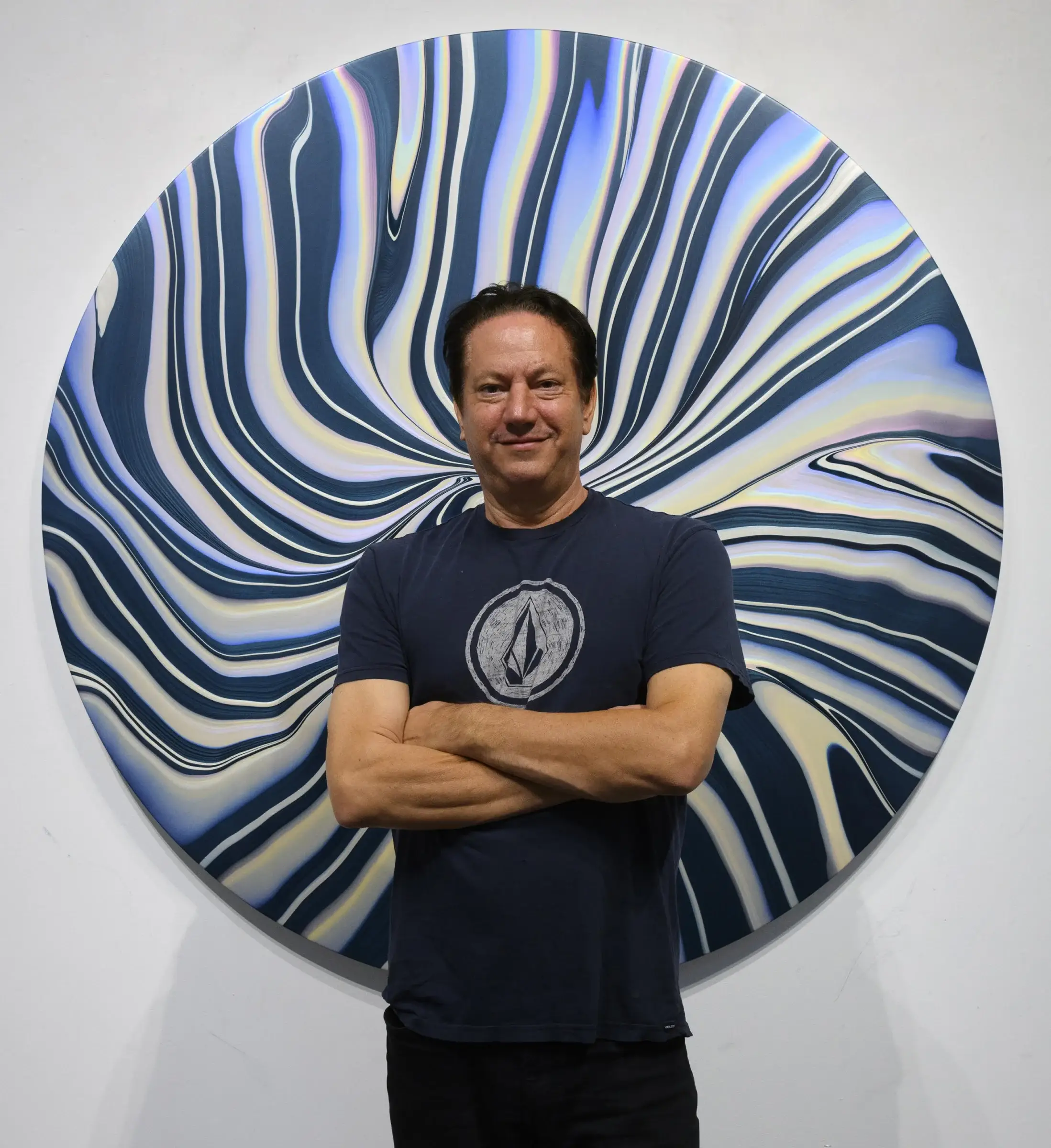 Andy Moses standing in front of one of his art pieces wearing a dark blue Volcom t-shirt.
