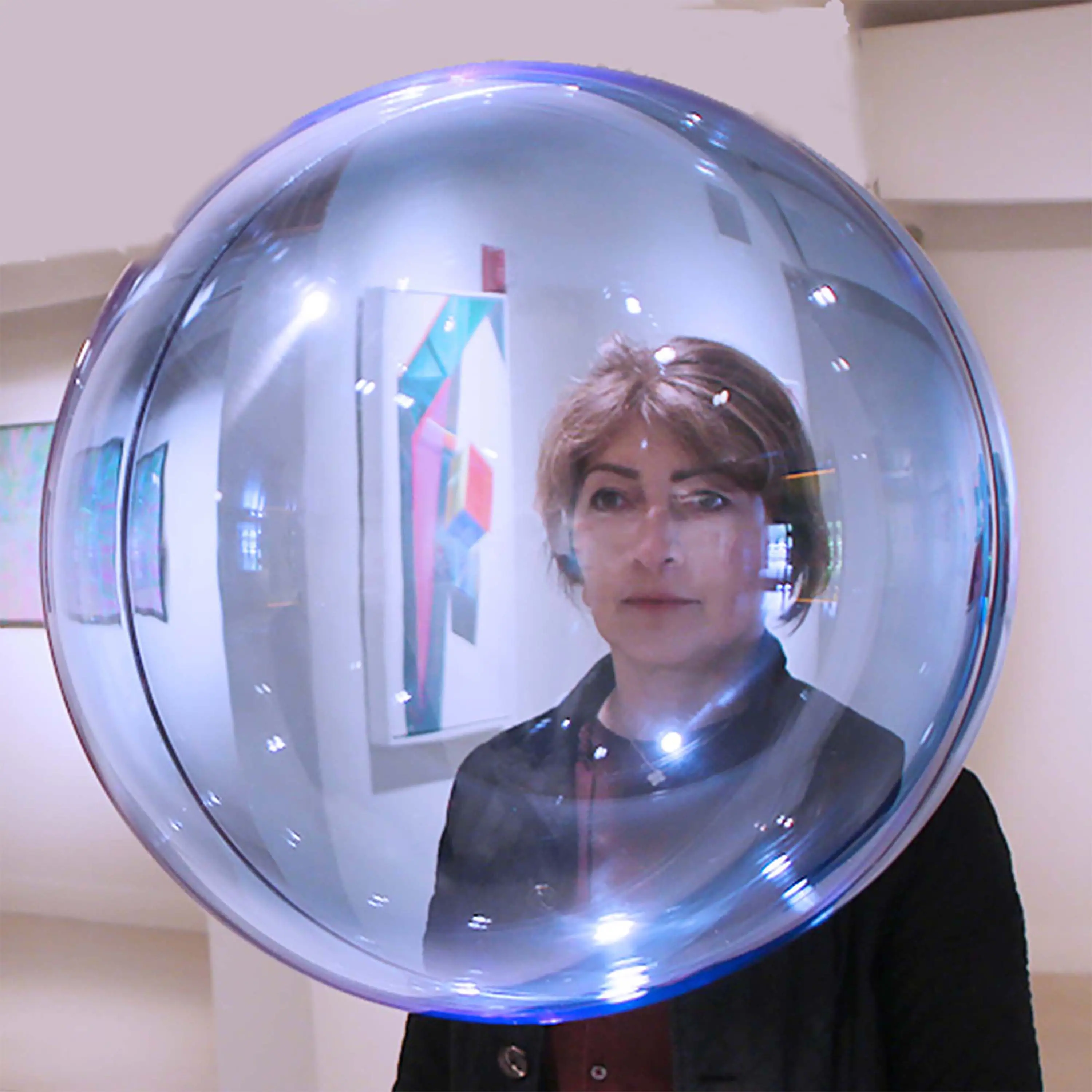 Woman with shoulder-length light brown hair standing behind a blue glass sphere that is warping her face.