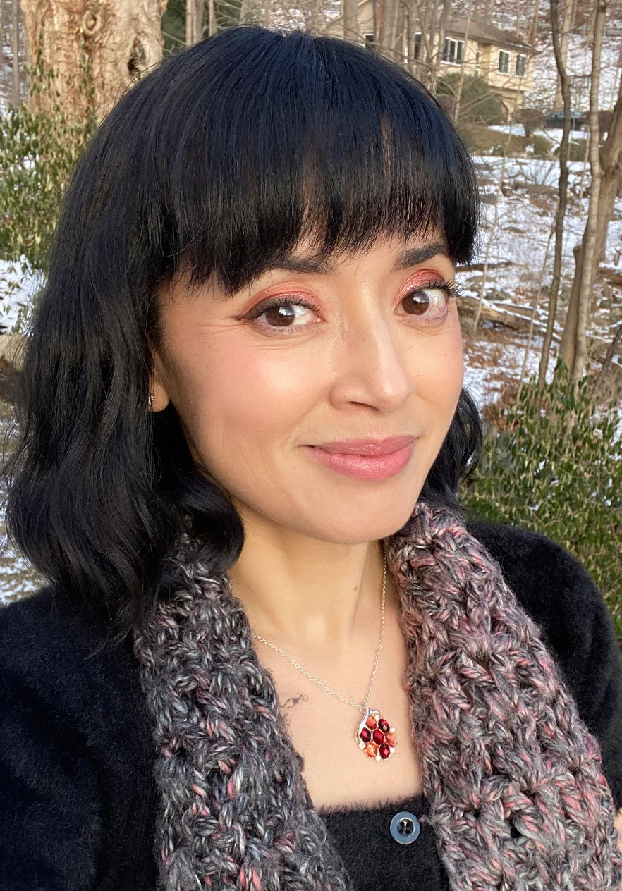 Woman with short dark hair and a soft fabric jacket smiles at the camera.
