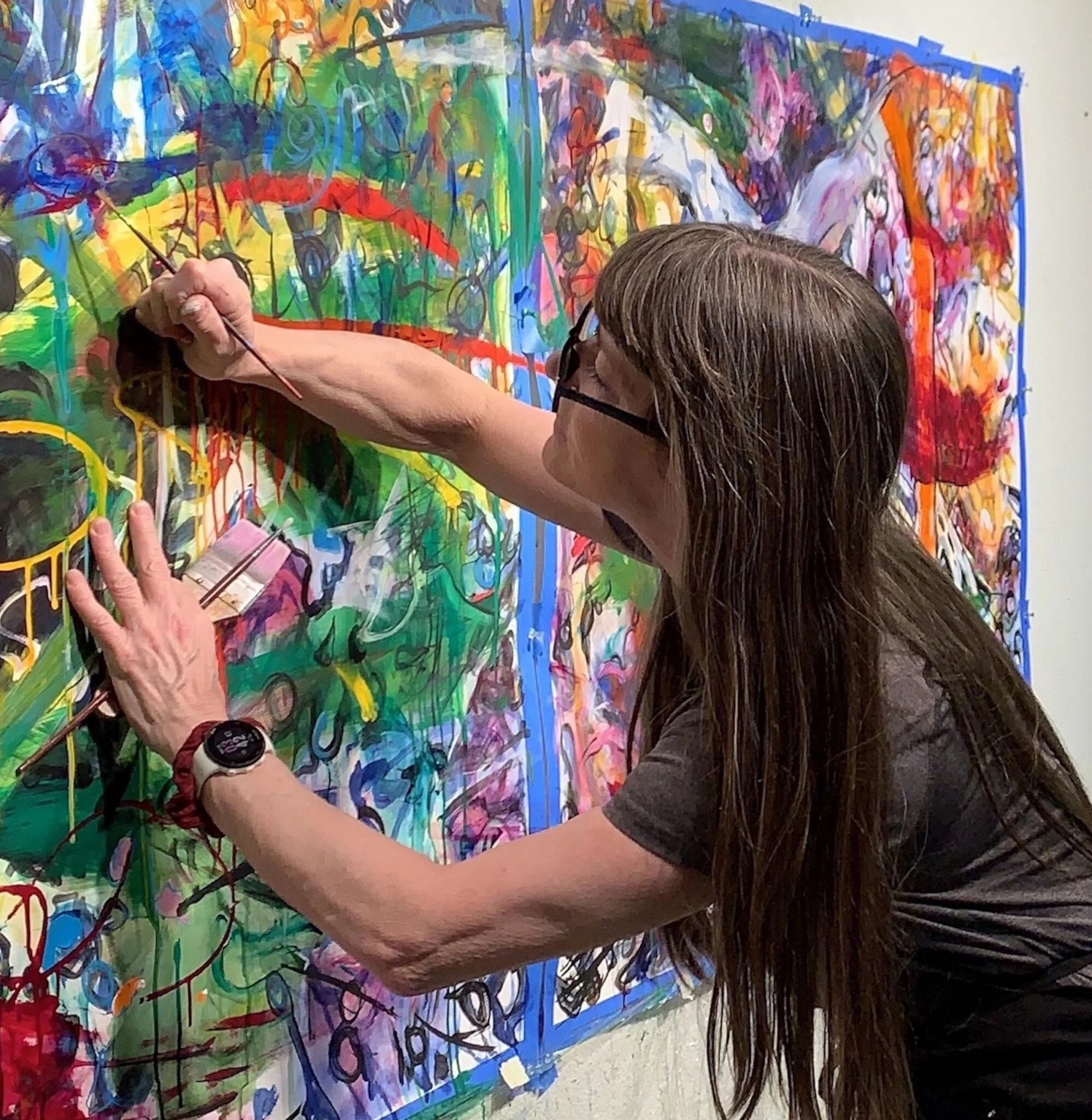 A woman with long brunette hair and glasses adds detail to an artwork.