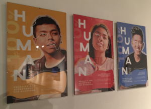 three posters, one blue, on yellow, and one red, each featuring a portrait of a person and the words 'human'