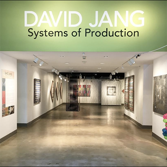 title wall of gallery painted green with white text that reads: David Jang and smaller black text that reads: Systems of Production. 