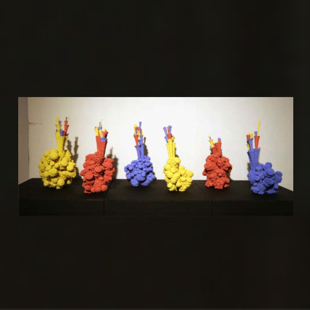 Three sculptures in shapes resembling test tubes. The surface of these sculptures in textured and bubbly. They are painted one red, one blue, and one yellow