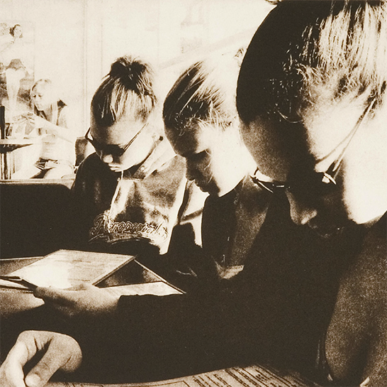 sepia image of three women looking down a menus at a table.