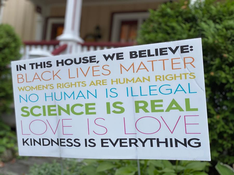 Lawn sign with multicolored lines of text that read: In this House, we believe: Black Lives Matter, women's rights are human rights, no human is illegal, science is real, love is love, kindness is everything.