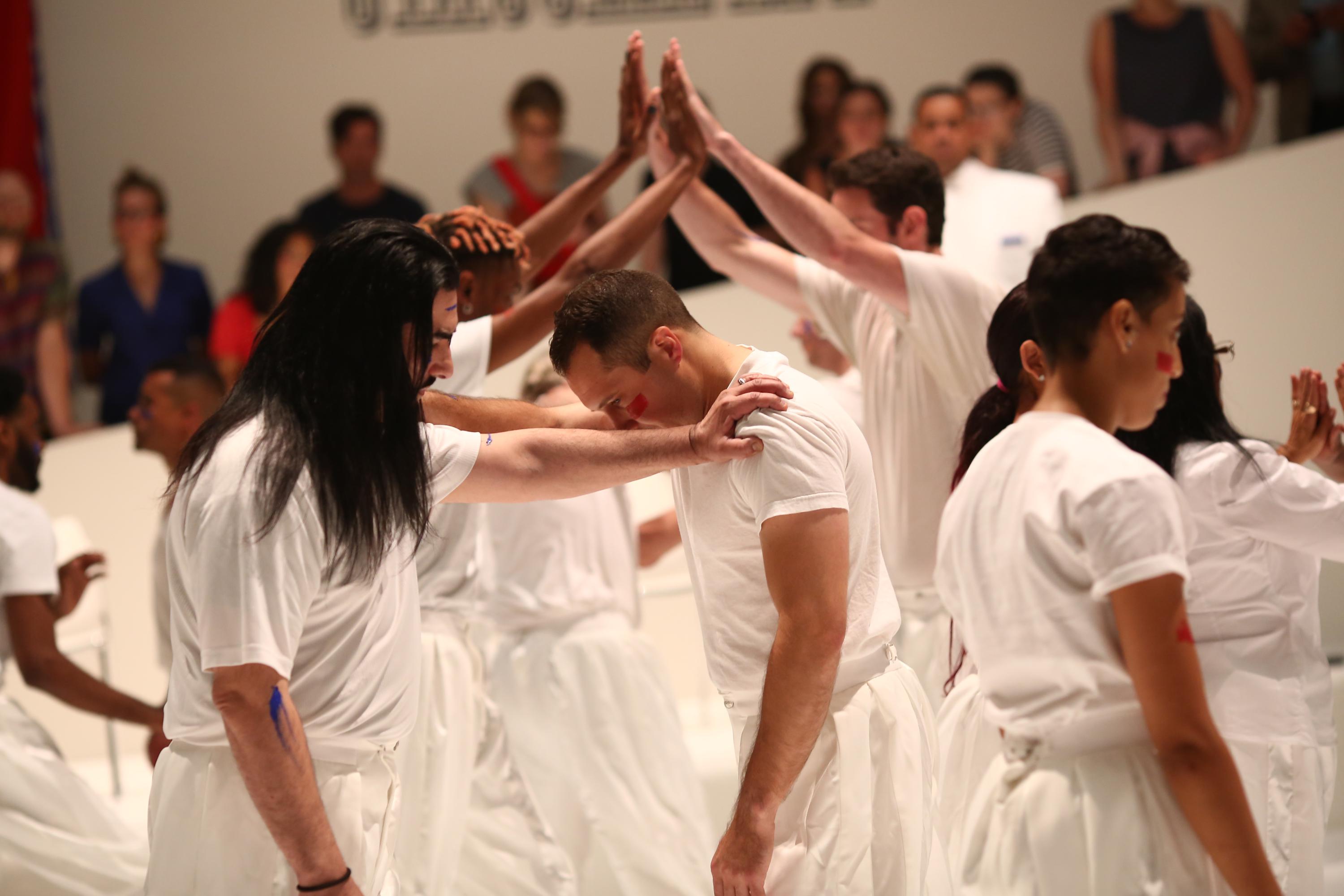 Image of people in white clothing with hands up, creating an arch. Caption:Primitive Games - performance, 1 hr. at Guggenheim Museum, New York, NY, 6/21/18. Photo by Paula Court" 