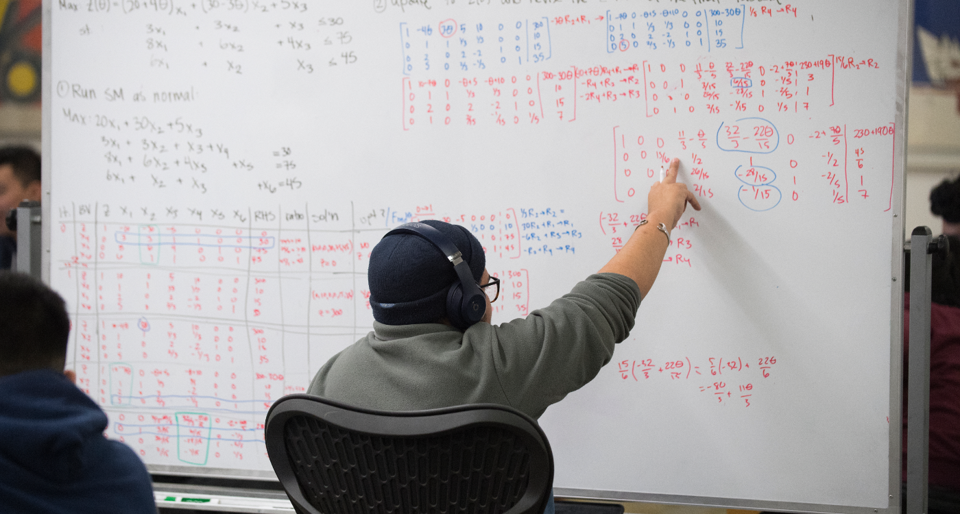 A student points at math on a whiteboard