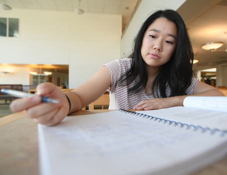 Student studies at a desk with a notebook and textbook