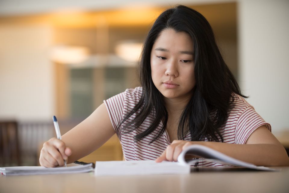 Student studies at a desk with a notebook and textbook