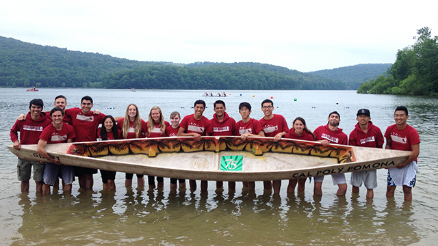 The Cal Poly Pomona Concrete Canoe team standing in a lake, holding up its canoe.