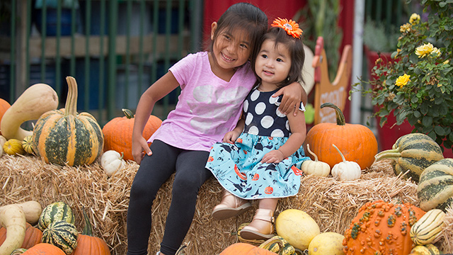 Two girls sitting on hay barrel.