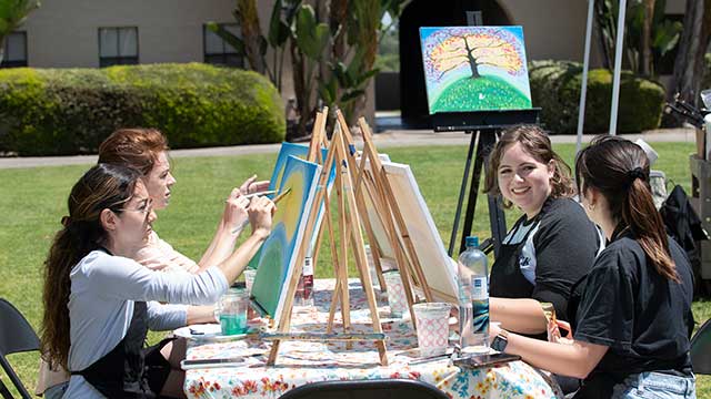 Students painting on canvas in the plaza.