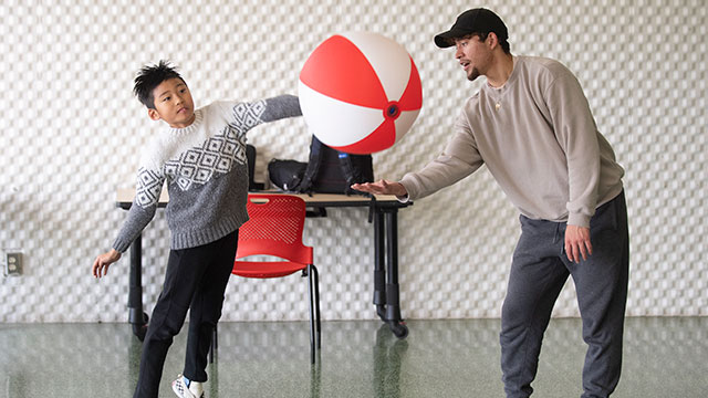 A student works with a child playing with a beach ball.