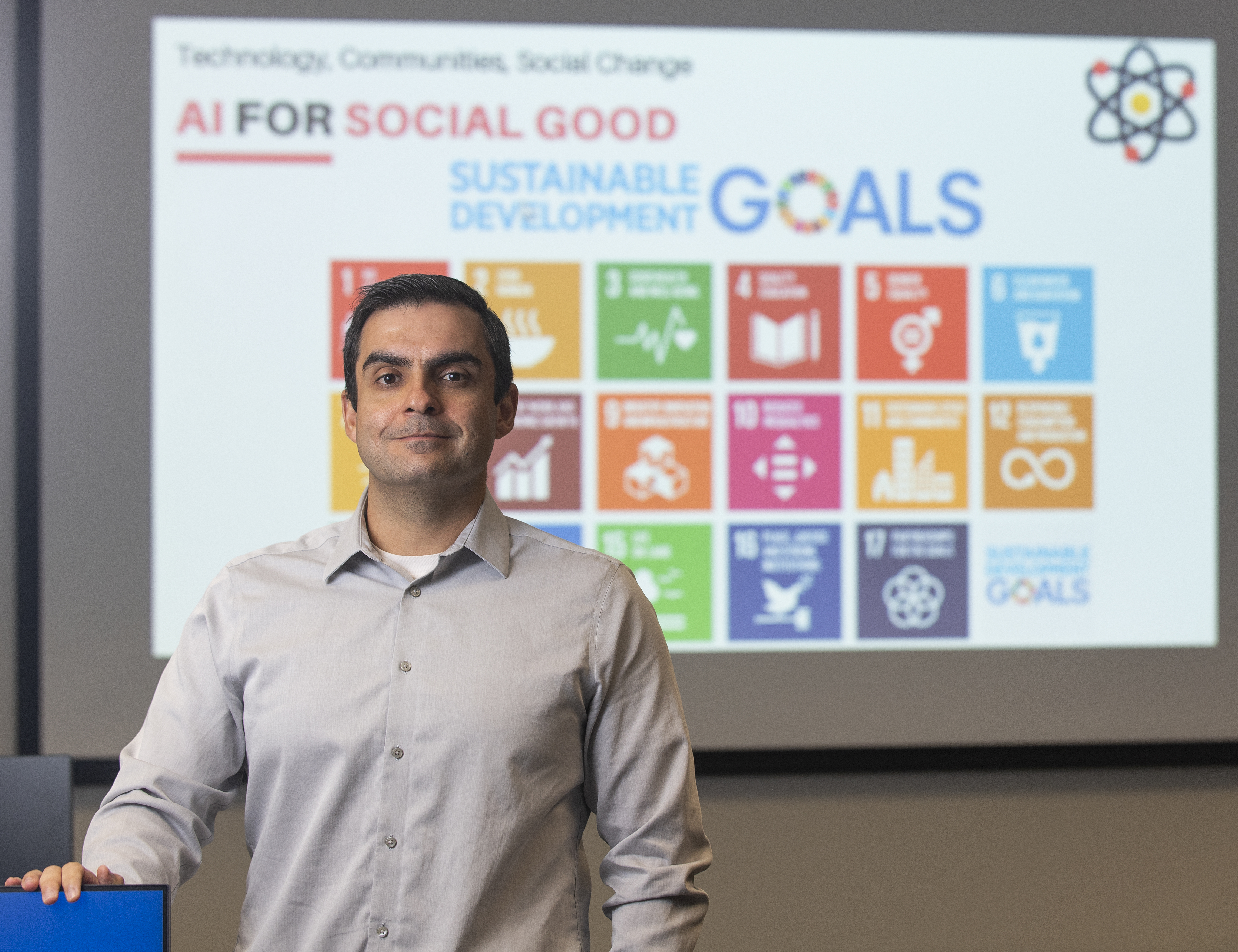 eography Assistant Professor Gabriel Granco stands in front of the AI for Social Good presentation showing all 17 of the UN Sustainable Development Goals