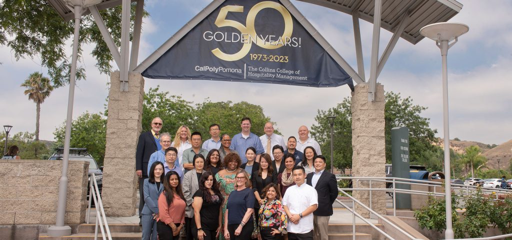 Collins College of Hospitality Management staff pose in front of a 50th Anniversary banner.