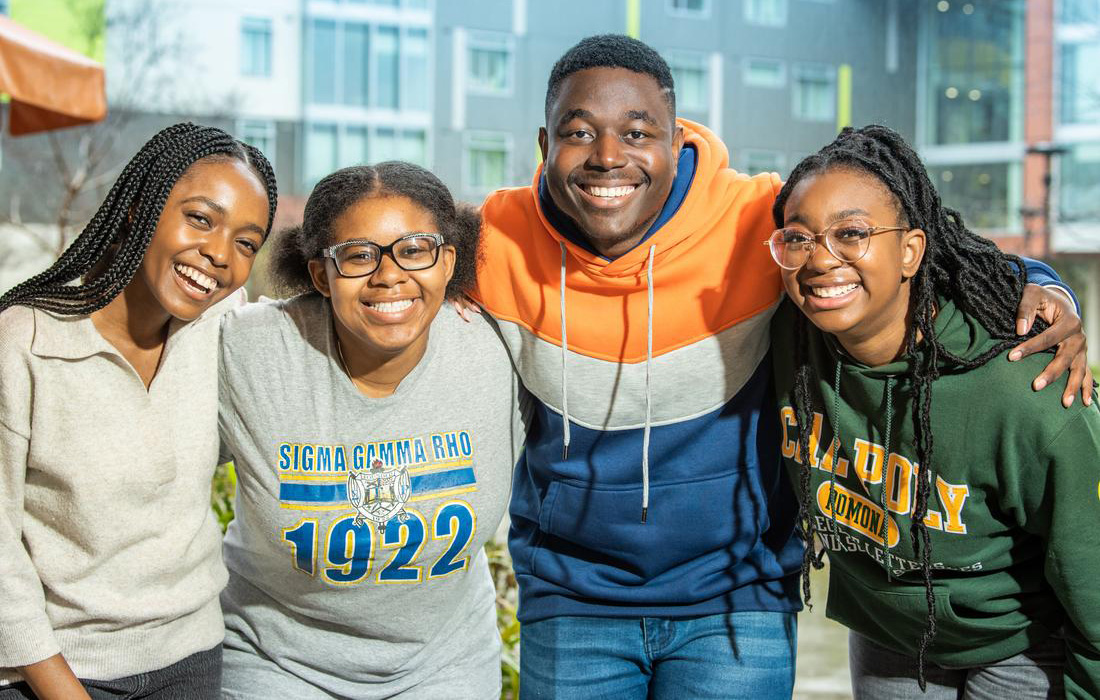 A group of black students smile and hug each other.