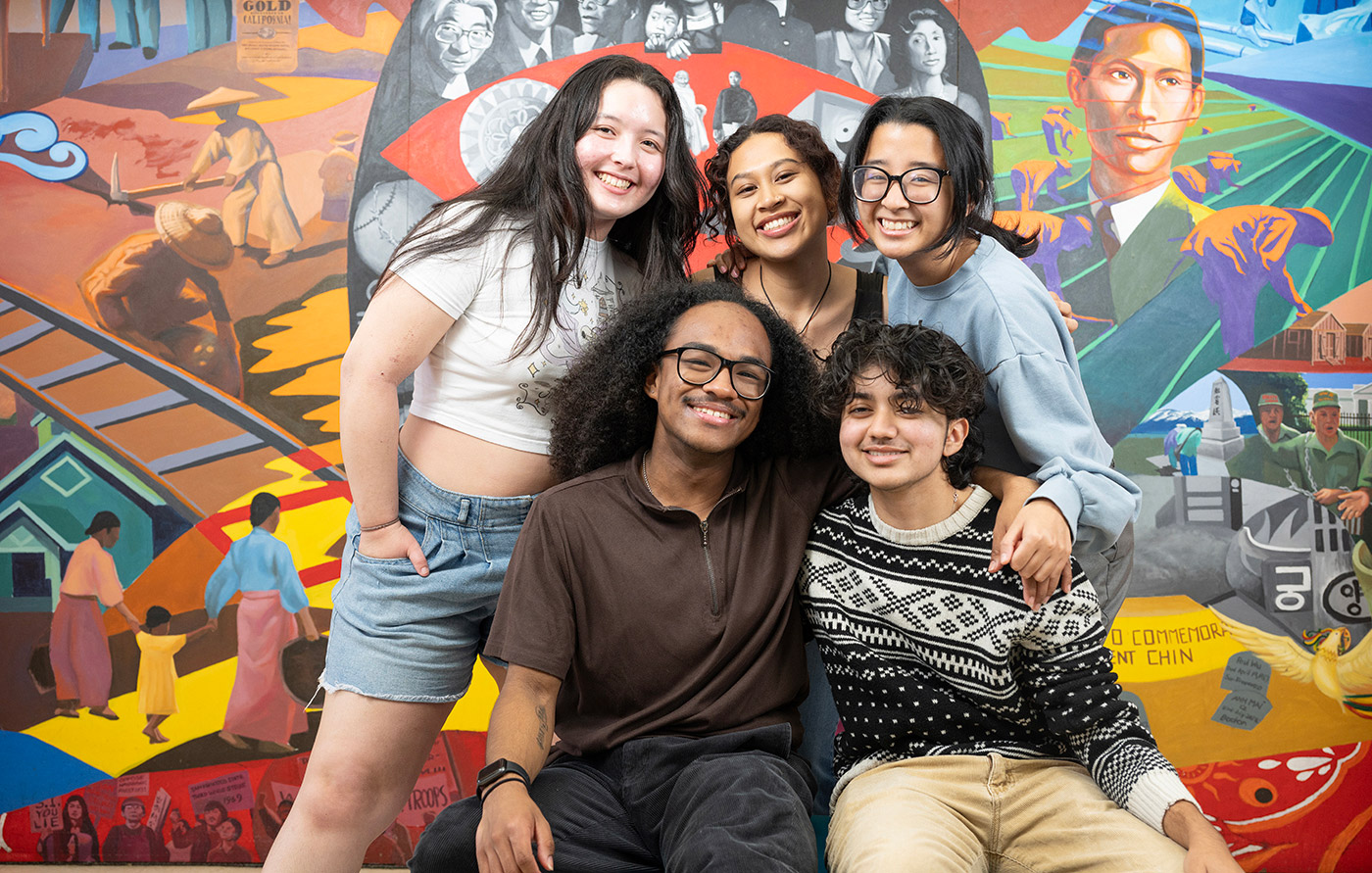 Students pose in front of a mural inside the Asian and Pacific Islander Student Center