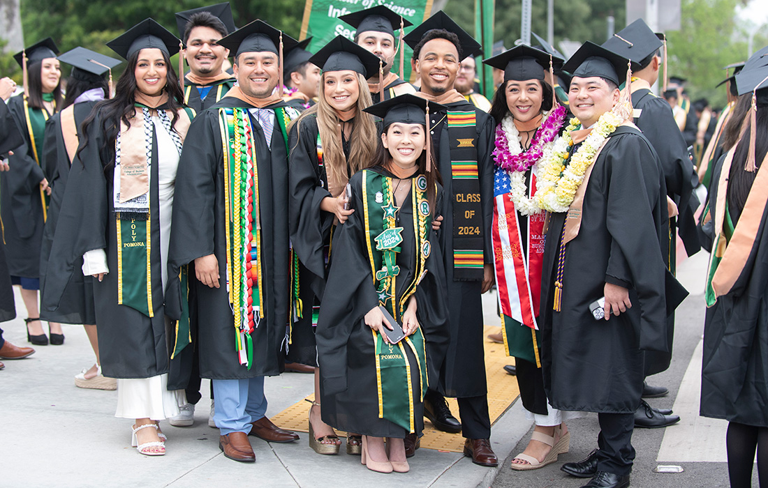A group of grads from the College of Business smile during the 2024 commencement ceremonies.