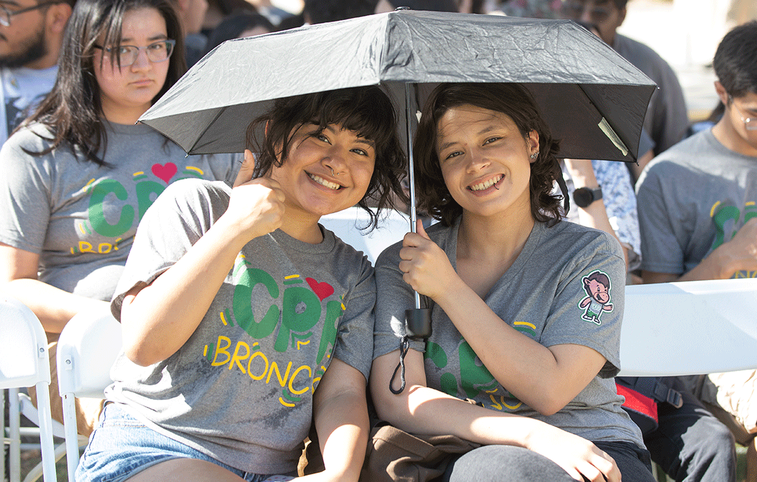 Two female students share an umbrella for shade