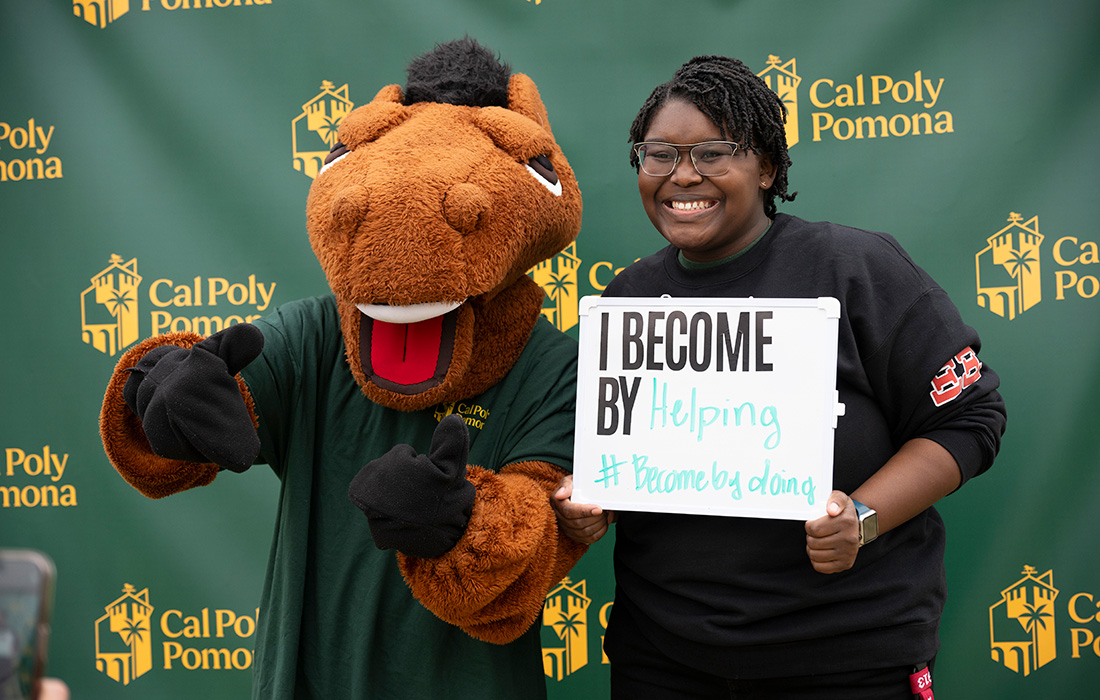 Student with Billy Bronco holds a sign that says I Become by Helping