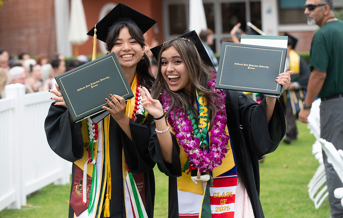 Two Female College of Ag students smile while holding diplomas