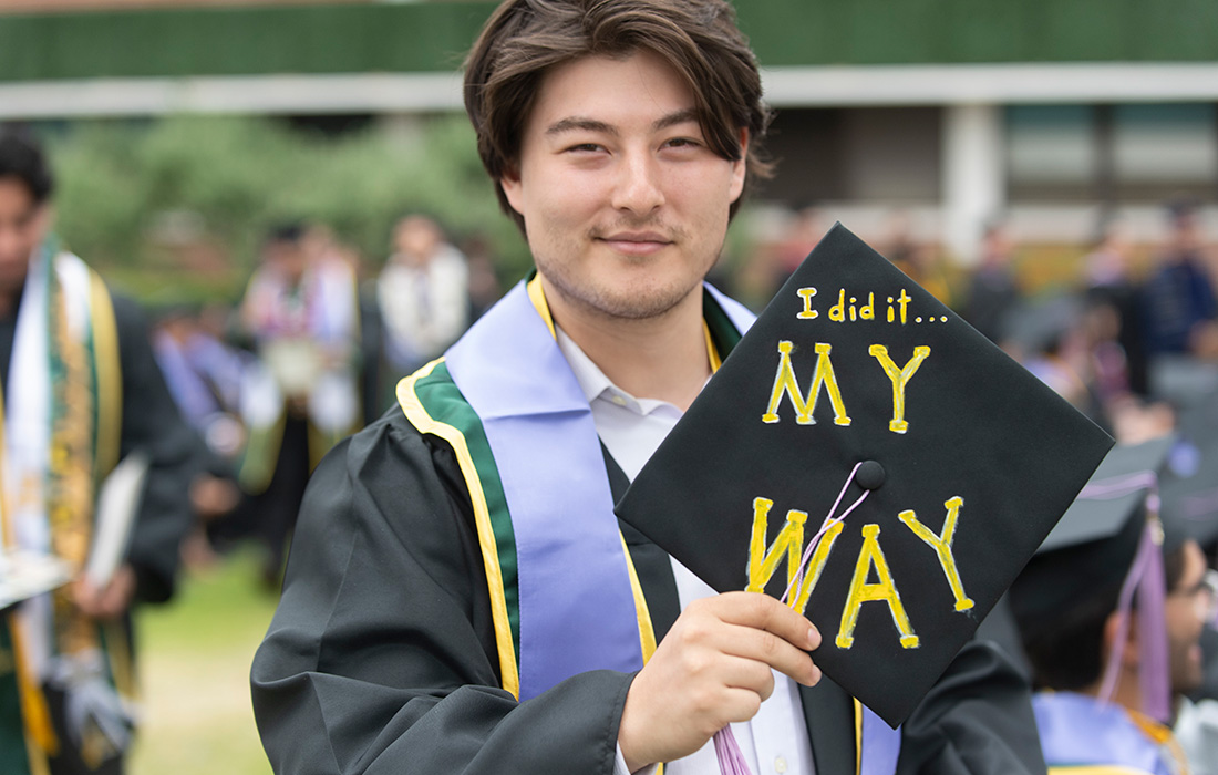 Male graduate holds his mortarboard that says I Did It My Way.