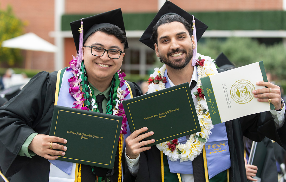 Two male College of Environmental Design students hold their diplomas.