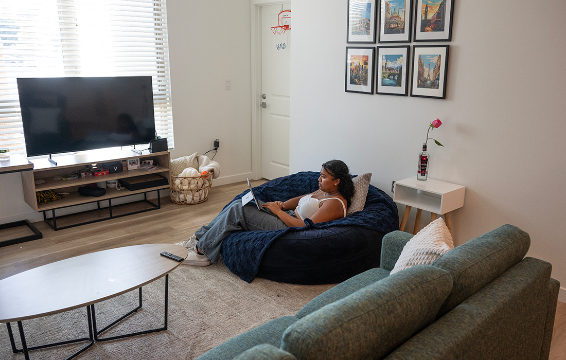 A student sits on a chair in a dorm room. 