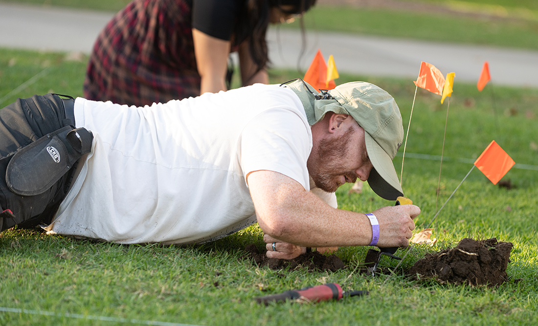 A male student lays on the grass while excavating