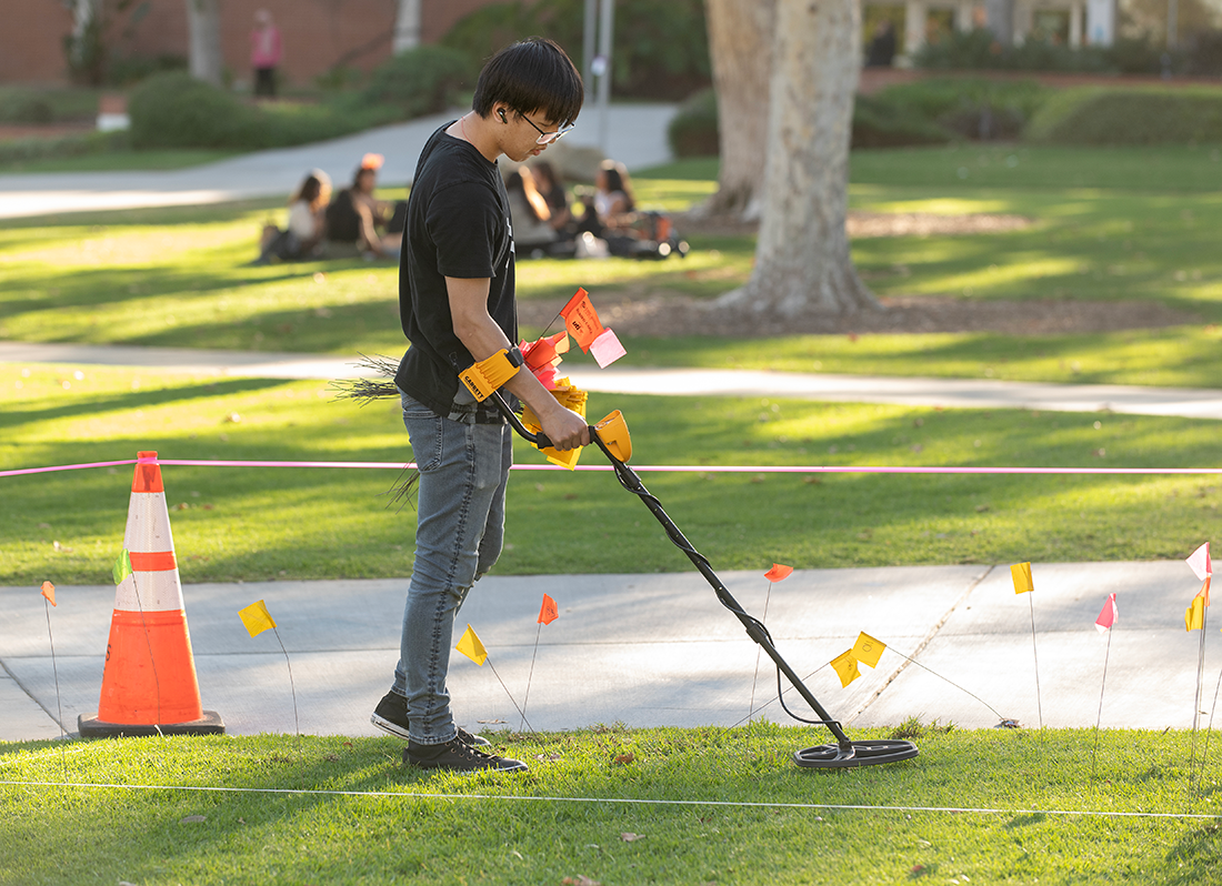 A student uses a metal detector on the quad