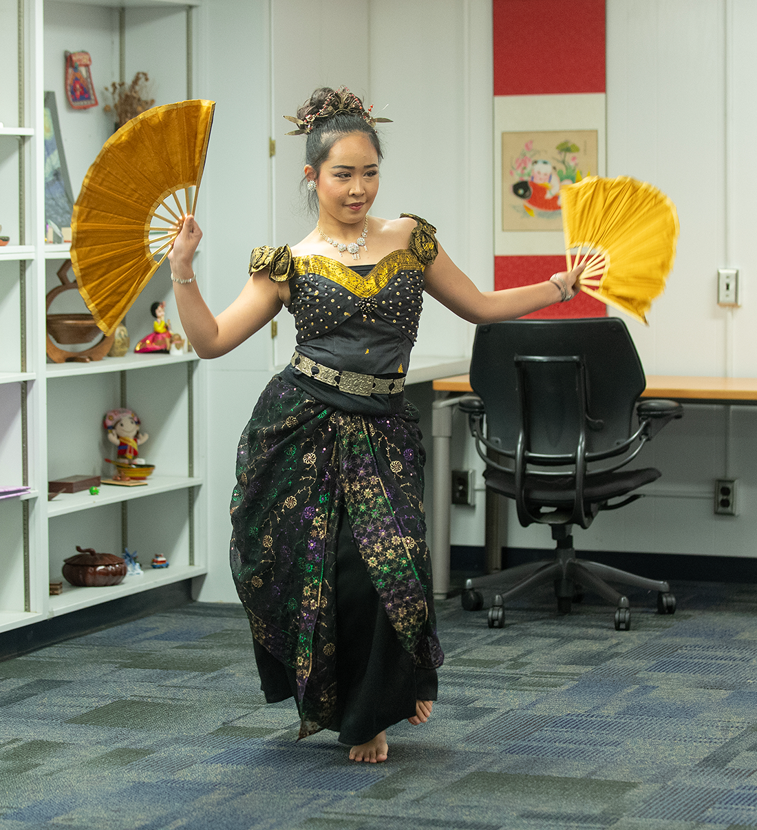 Female dancer in traditional costume holding two yellow fans.