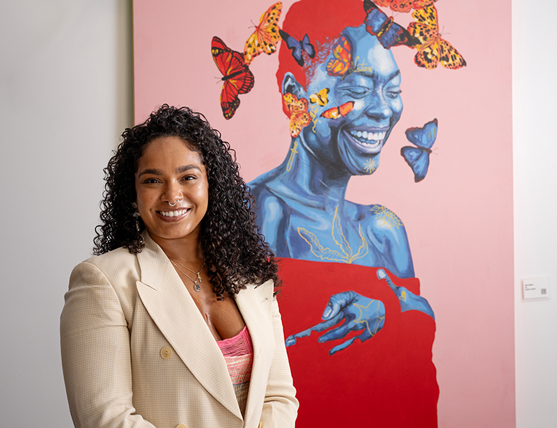 Perri Lawler in front of one of her creations of a black woman smiling surrounded by Butterflies.