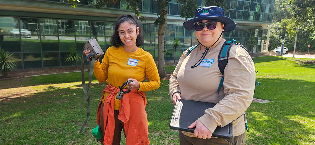 Two Womxn in the Wild smile with Camera Traps in hand.