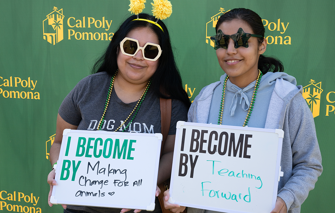 Two students pose for a photo while holding Become by Doing signs